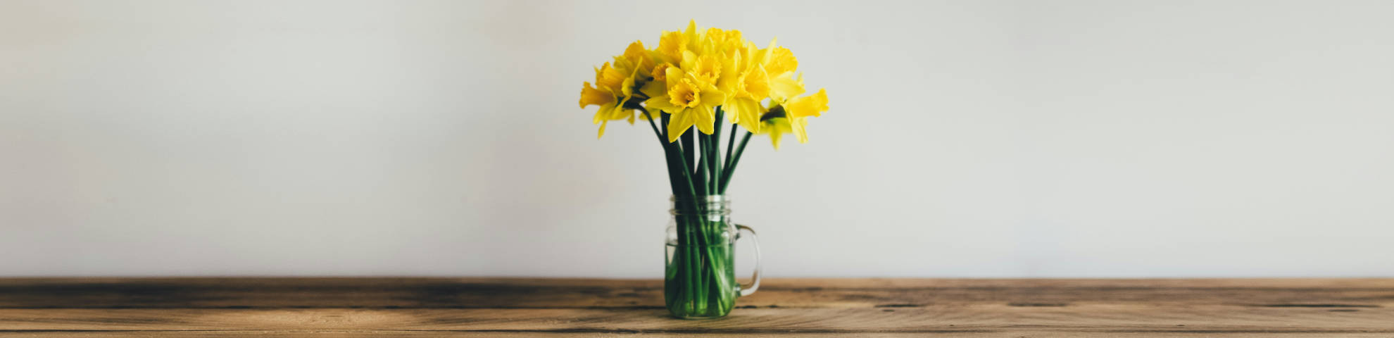 A bunch of daffodils in a glass vase on a wooden table